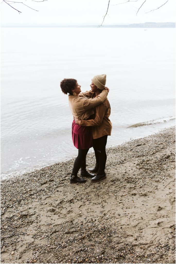 An LGBTQ+ couple embraces on the shore of Puget Sound during their Point Defiance engagement session