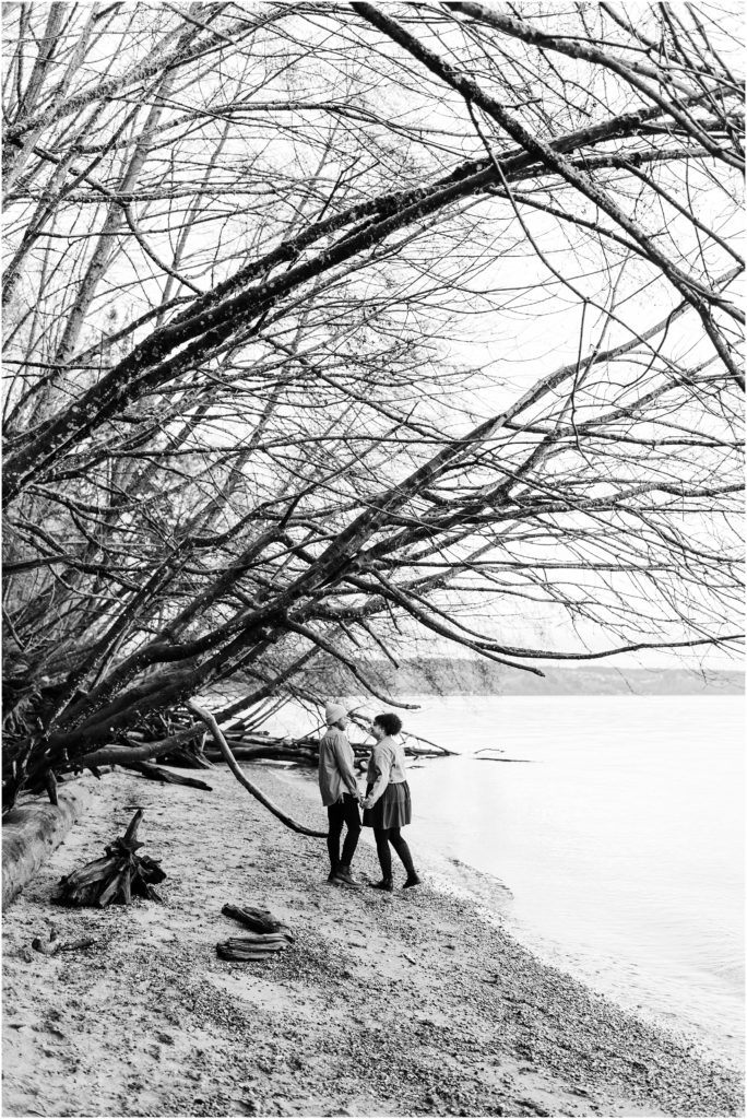 An LGBTQ+ couple embraces on the shore of Puget Sound during their Point Defiance engagement session