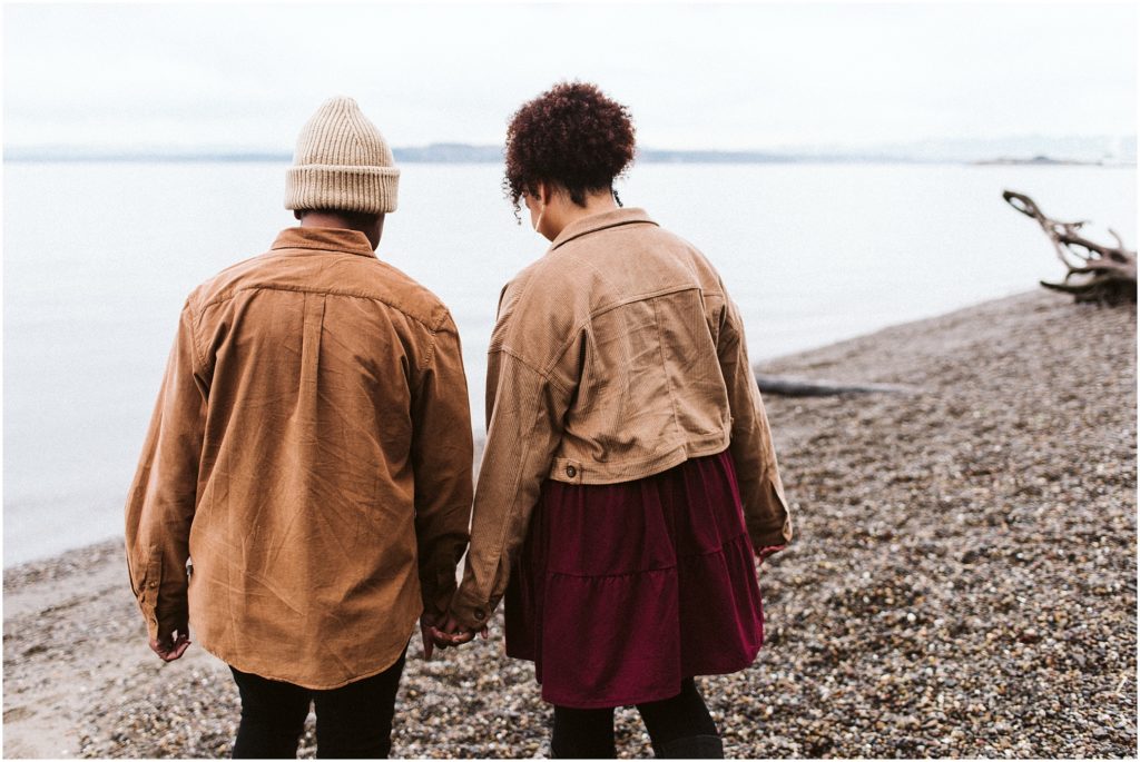 An LGBTQ+ couple holding hands on the shore of Puget Sound during their Point Defiance engagement session