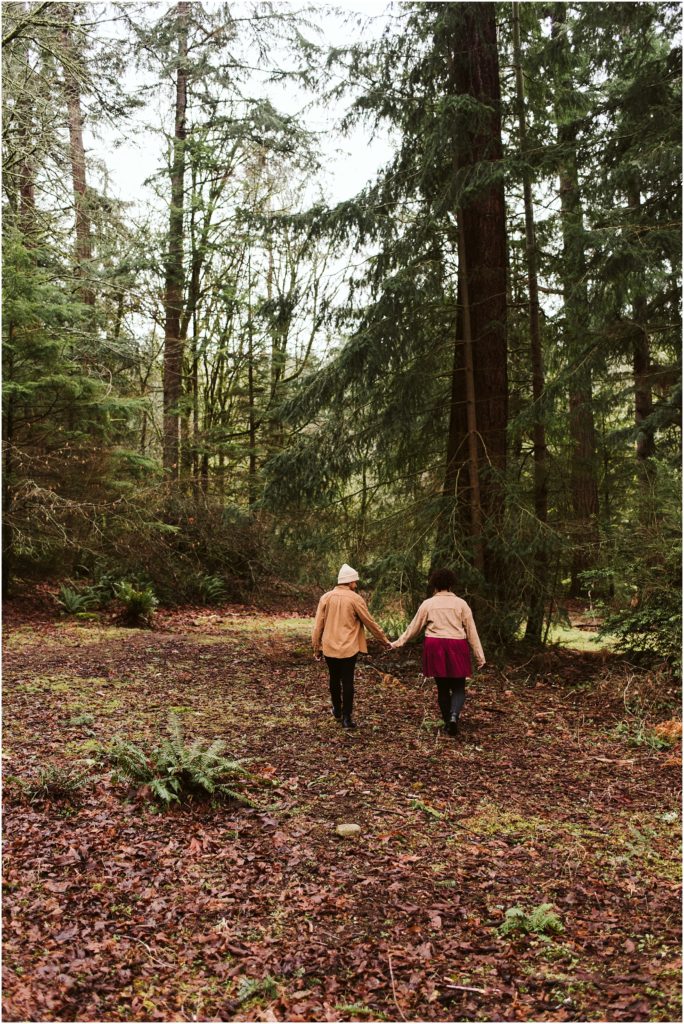 An LGBTQ+ couple walking through the forest, holding hands, during their Point Defiance engagement session