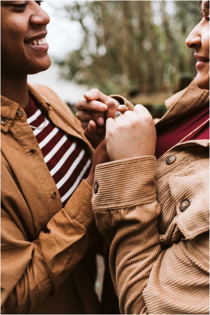 An LGBTQ+ couple holding hands close to their chins and smiling during their Point Defiance engagement session