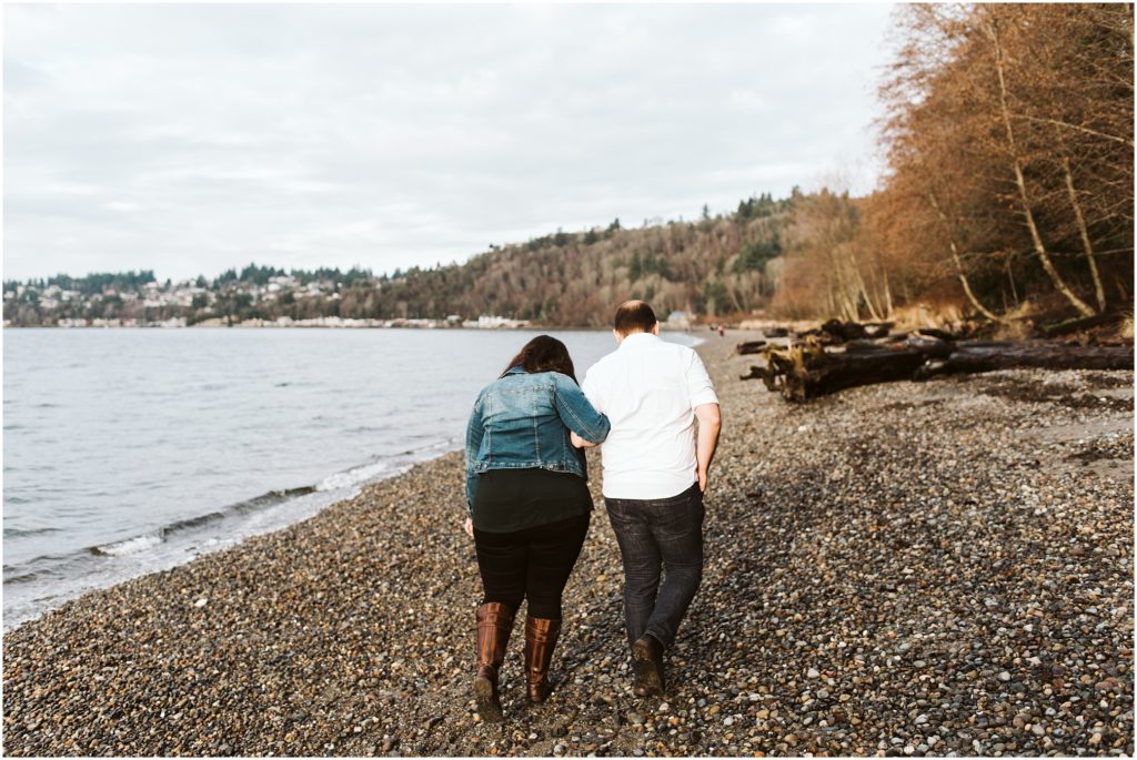 An engaged couple walking along Puget Sound, arm in arm, for their Seattle engagement photos