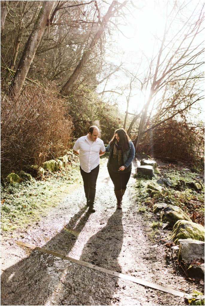 An engaged couple walking up a forest trail, arm in arm, during their Seahurst Park engagement session
