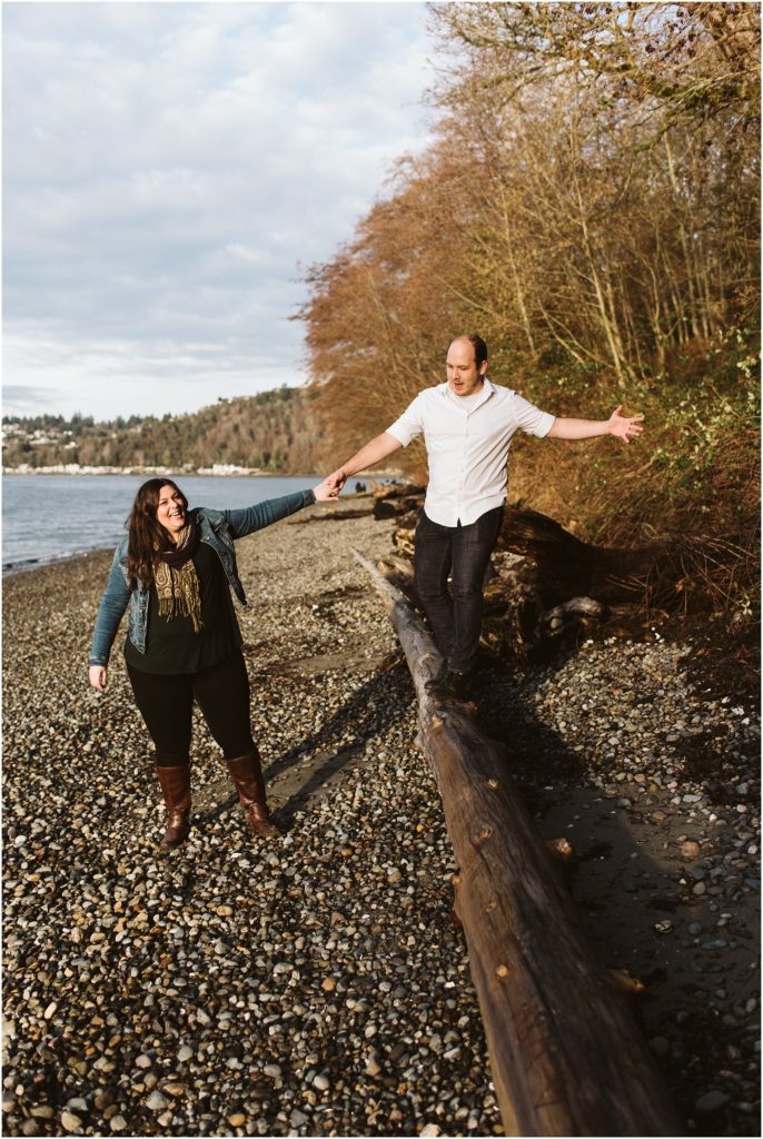 An engaged couple playing on a log on Puget Sound during their Seahurst Park engagement session
