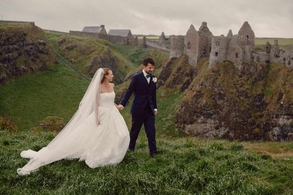 A married couple walks together in front of Dunluce Castle for their wedding